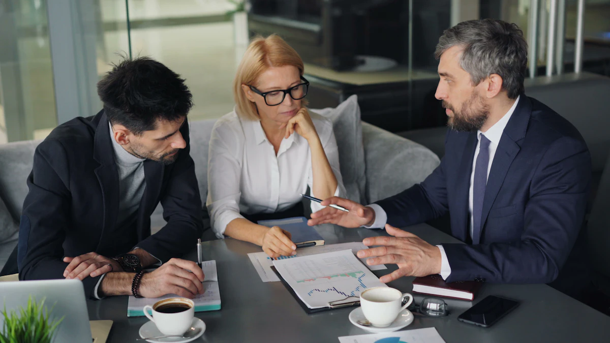Three people in conversation around a table with papers and coffee cups.