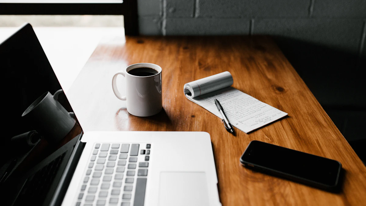 A laptop, coffee mug, notepad, and phone on a wooden desk.
